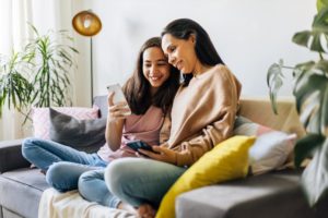 mother and teenage daughter sitting together on couch looking at a phone about family therapy techniques for communication