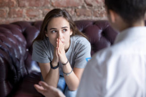 adolescent girl sitting on couch in front of therapist wondering have i experienced trauma