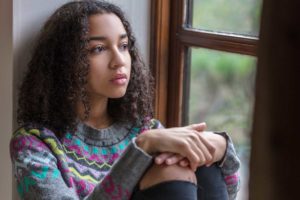 teenage girl sitting against wall staring out the window wondering how common is depression in teens who are bullied