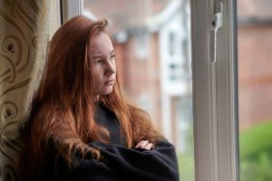 grumpy teenage girl staring out window displaying one of the 10 signs your teen needs therapy