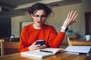a teenage girl gestures distraughtly at her phone as an indication of one of 5 sings your teen is in a a manipulative relationship