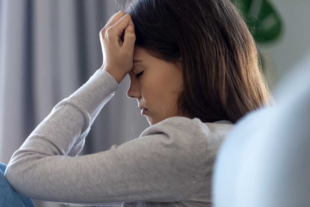 teenage girl sitting in a chair with her head cradled in her head employing one of 5 strategies for coping with trauma as a teen