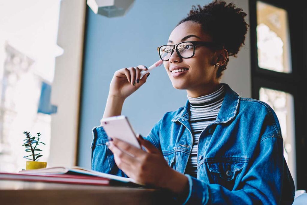 smiling teenage girl seated at school desk looking at phone to discover how to help change teens negative thinking patterns