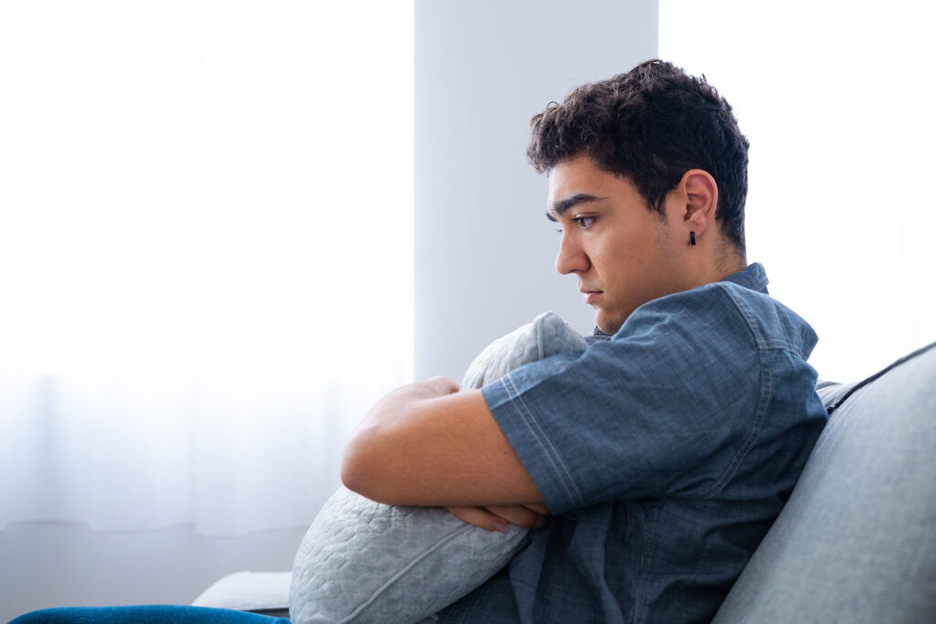 teenage male looked stressed and hugging a pillow while seated on couch displaying one of 5 signs and symptoms of anxiety in teens