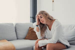 a teen sits on a couch holding their head as they deal with common signs of emotional trauma in teens