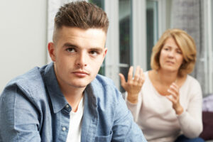 image of teenage boy with distraught mother in the background wondering how to plan an intervention for your teen